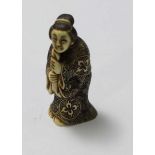 A Japanese Meiji Period Carved and stained Ivory Netsuke figure of an elderly lady clutching a piece