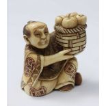 A Japanese Meiji Period Carved and stained Ivory Netsuke figure of a man seated cross-legged with