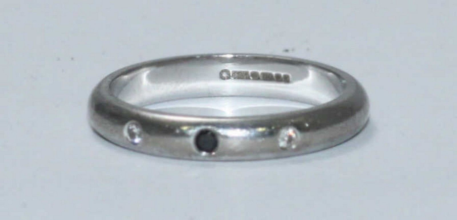 An 18ct white gold wedding ring, the band set with a small black diamond flanked by two small