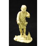 A Japanese Meiji Period Carved Ivory Okimono figure of a farmer holding a garden hoe, signed to