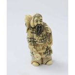 A Japanese Meiji Period Carved and stained Ivory Netsuke figure of an elderly man with a Kanji in