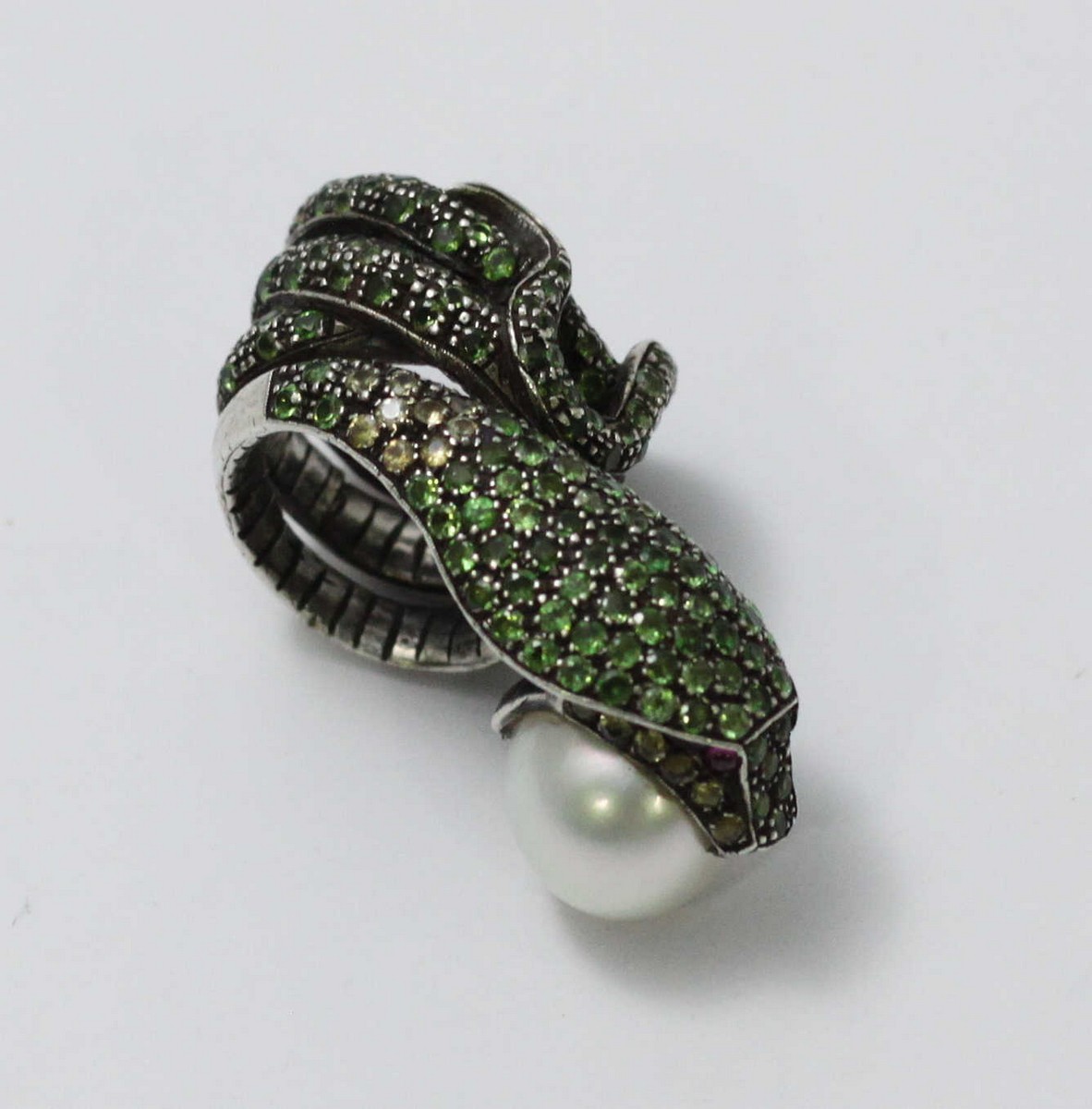 A white-metal ring modelled as a coiled snake, pave-set with green stones and holding a large