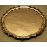 A large silver circular salver, with a raised moulded shaped border, on four leaf scroll feet,