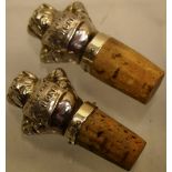 A pair of novelty wine corks of two hollow pigs as tops to corks, with repousse texts on their bibs,