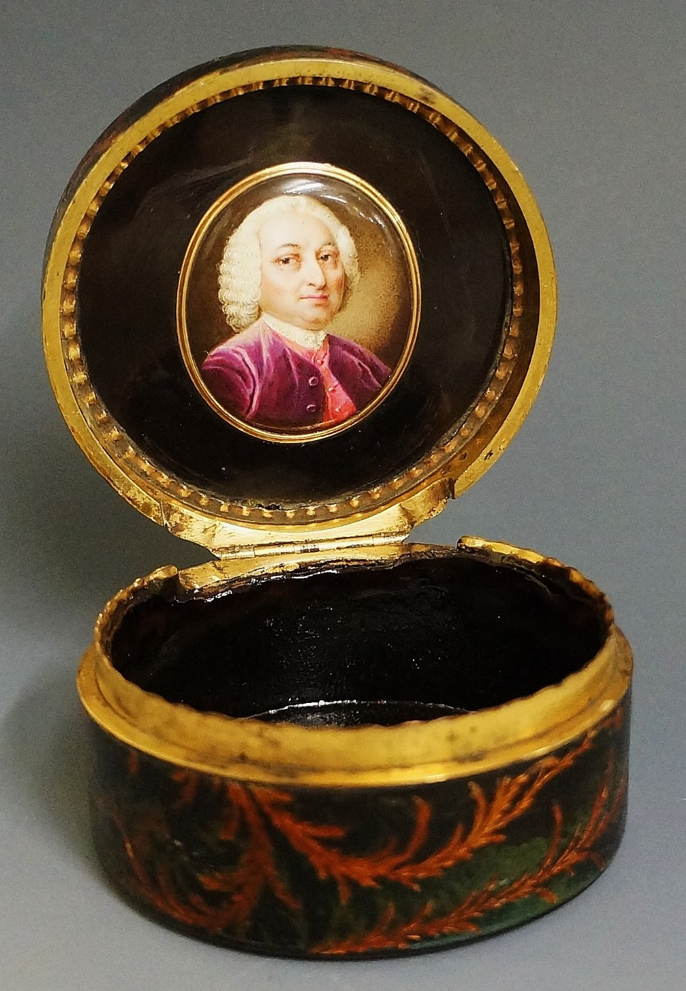 A 19th Century green papier maché circular box the hinged lid decorated with musical trophy and