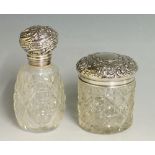 A silver topped dressing table jar, the silver lid chased and embossed with scrolling foliage,