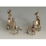 A pair of 19th Century Austrian? silver salts in the forms of cherubs driving elaborately cast and