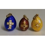 Three miniature Russian enamel egg pendants, enamelled in red, yellow and blue, gem set and inlaid,