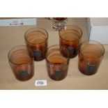 A set of five glasses with attached metal plaques depicting folklore,