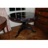 An ebonised circular Table with central turned pillar and three splayed feet with floral decoration,