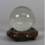 A crystal ball raised on a Chinese carved hardwood plinth.