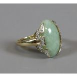 A 9ct gold ring set with an ovoid celadon jade table under Greek key diamond set, size Q.