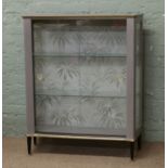 A painted 1950s china cabinet with sliding glass doors and raised on tapering supports.