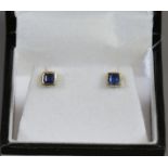 A pair of gold ear studs set with square set sapphires.