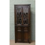 A carved oak corner cabinet with leaded glass doors.