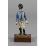 A cold painted bronze figure of a C19th soldier raised on a square wooden plinth,
