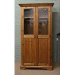 A modern pine two door wardrobe with partly glazed and panelled doors raised on bracket style feet