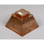 A copper inkwell of square tapering form and decorated with leaf scrolls.