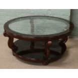 A two tier mahogany circular coffee table with glass top and raised on carved scroll supports.