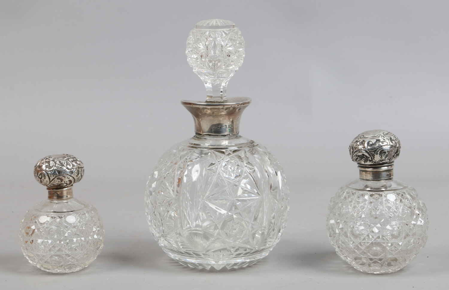 A large cut glass globular scent bottle and stopper with silver collar and two similar small