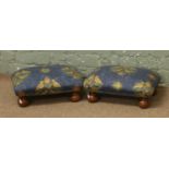 A pair of floral upholstered foot stools raised on squat bun feet.