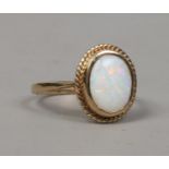 A 9ct gold opal dress ring with ovoid stone under a ropetwist border, size L.