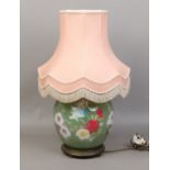 A large pottery based tablelamp with painted floral design with pink tasselled shade.