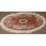 A pink ground oval thick pile hearth rug with floral decoration.