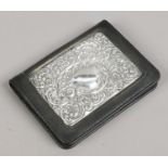 A silver mounted black leather notebook holder with chased scrollwork decoration,