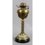 A brass based oil lamp with twist decoration raised on a glazed pottery plinth.