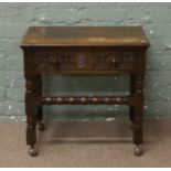 An oak carved and turned single drawer occasional table, raised on casters.