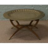 A large Indian brass top table on folding wooden base.