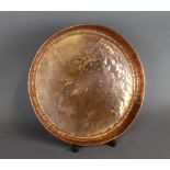 An early 20th Century hand beaten circular copper dish of Arts and Crafts design, possibly Keswick