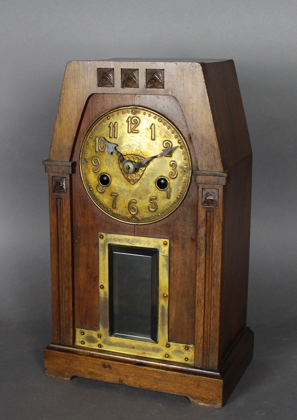 An early 20th Century walnut and brass mantel clock of Arts & Crafts architectural design, with