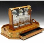 Late Victorian pale oak tantalus with applied Gothic brass mounts, of three square cut glass