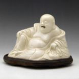 Chinese white glazed Fukian figure of the sitting Budai, width 21cm, on wooden base, Qing dynasty