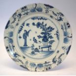 Delft charger circa 1750, painted with a lady standing beside a vase of flowers, 33.5cm diameter