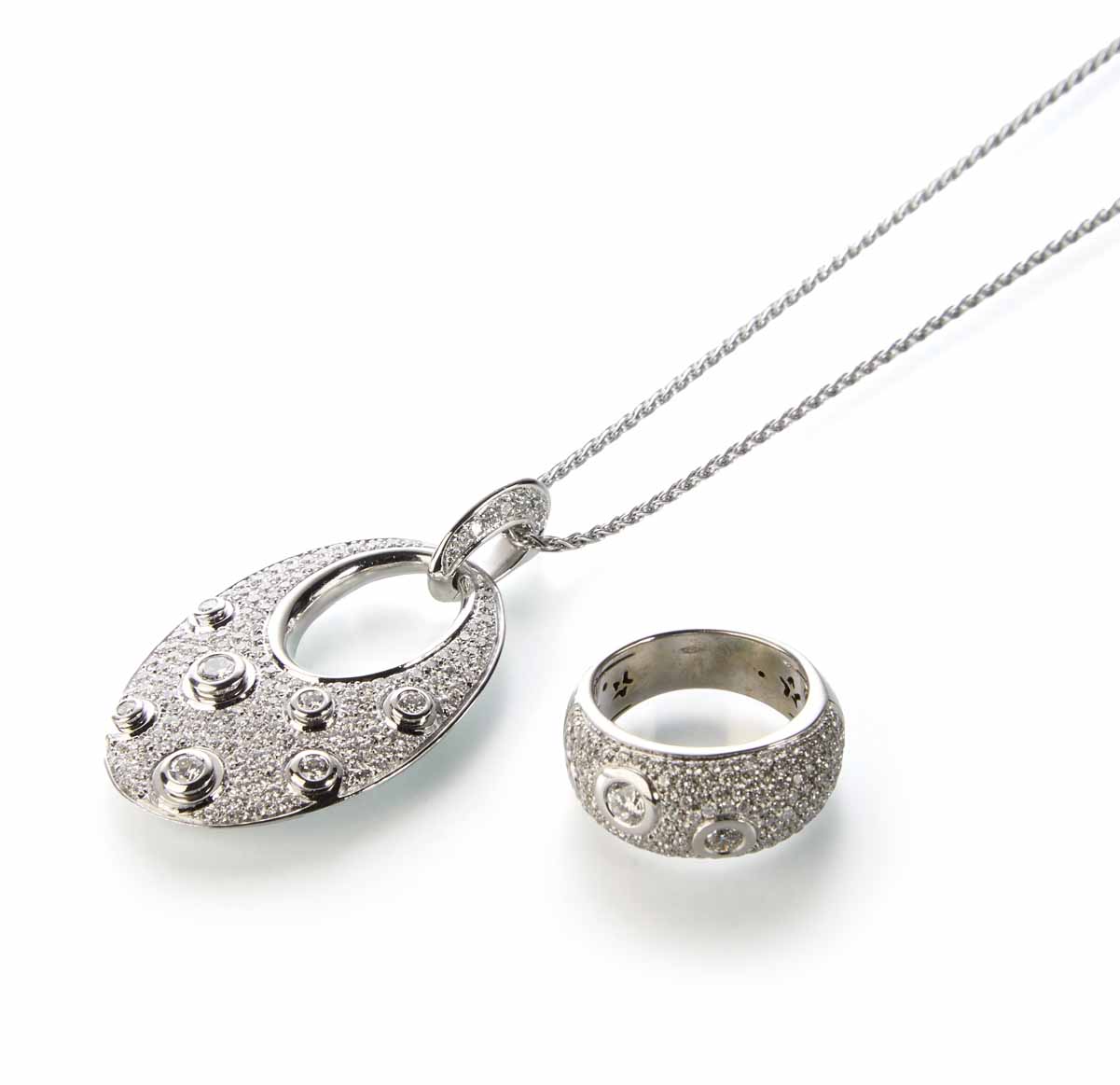 An 18ct white gold pave set diamond pendant and chain with matching ring. The oval modern design