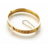 An Edwardian 15ct gold ruby and seed pearl set hinged bangle, a cross of small seed pearls to centre