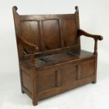 An antique oak box seat settle, with triple panelled back, open arms,