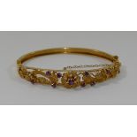 A 9 carat gold garnet set hinged bangle, with floral openwork design,
