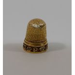 A yellow metal thimble, with bark-like decoration, the base decorated with a band of wire symbols,