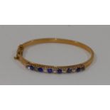 An early 20th century French gold hinged bangle set with a mixture of thirteen round mixed-cut blue