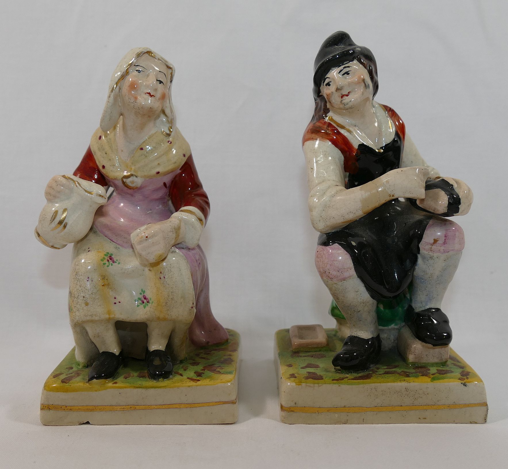 A pair of Staffordshire pottery seated figures of a man cleaning shoes and a woman with jug and cup,