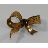 A 9 carat gold bow brooch, set with a single round mixed cut garnet, London 1963, 4.5cm wide, 8.