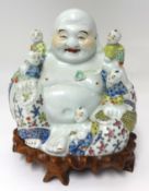 A early 20th Century porcelain Buddha and boys group with original carved hardwood stand, height