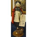 A Victorian peddler doll in period dress with basket and bag of her wares, under a glass dome
