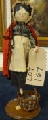 A Victorian peddler doll in period dress with basket and bag of her wares, under a glass dome