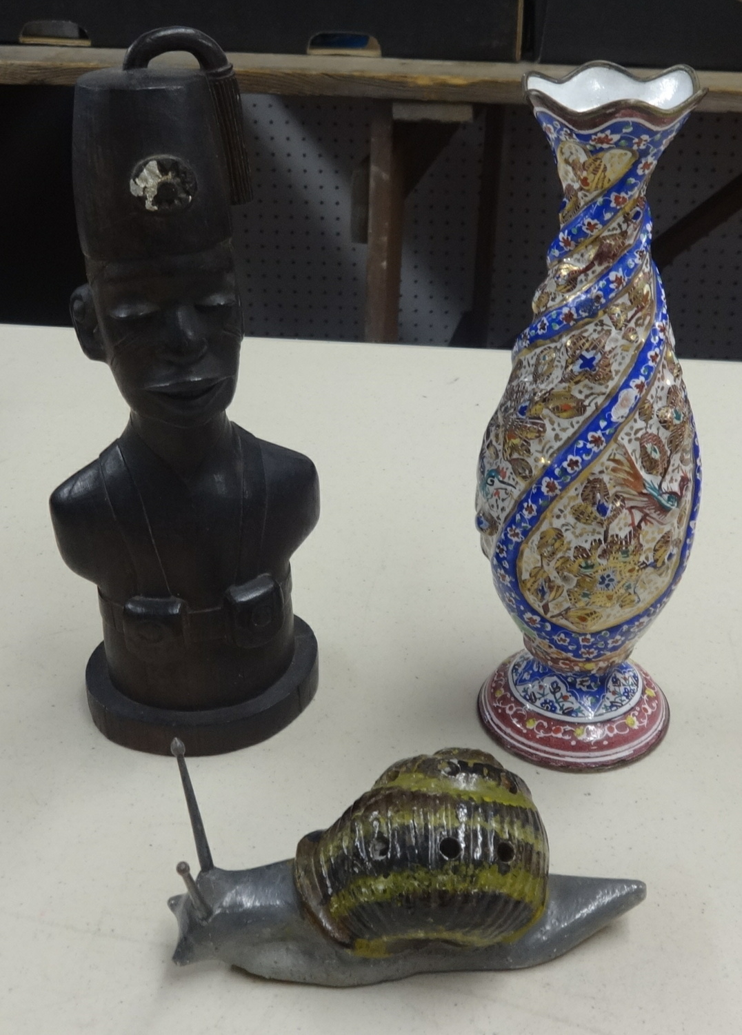 An ornate enamel decorative vase, a carved wood figure of an African and a stoneware snail model.