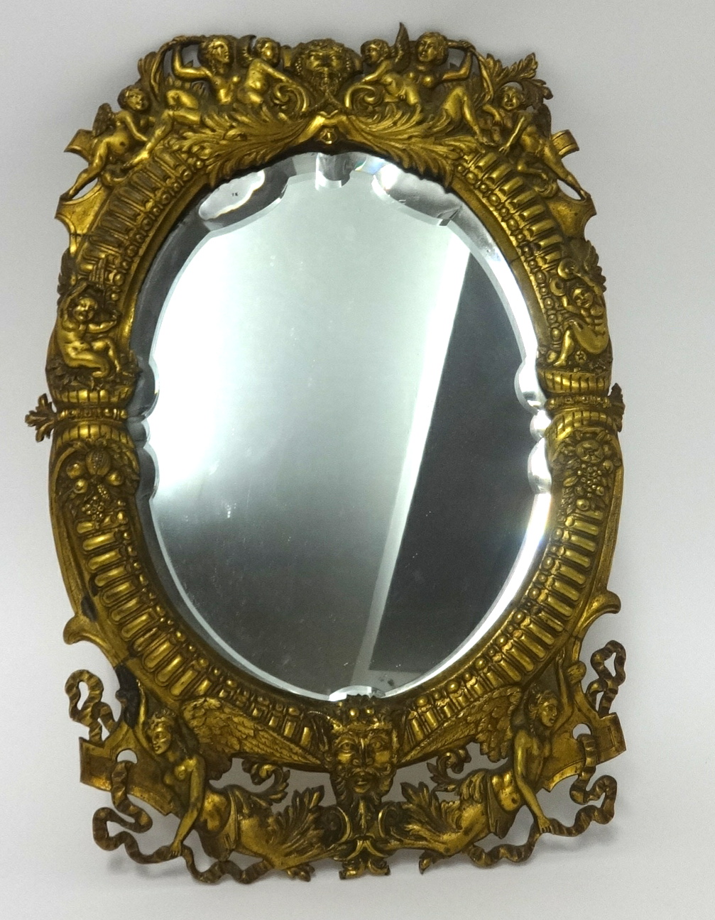 A gilt metal wall mirror, the ornate frame decorated with figures, cherubs, masks and ribbons,